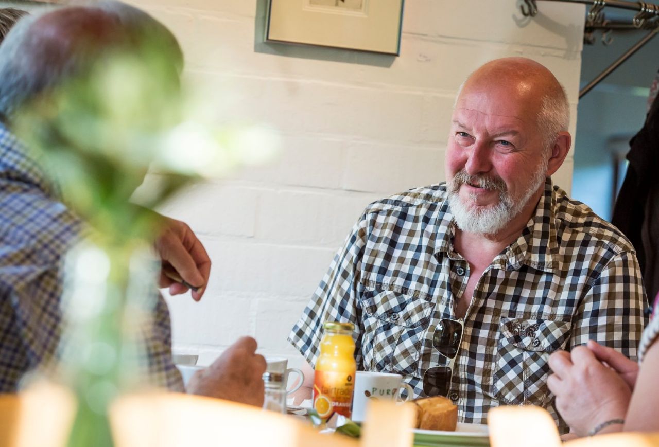 Twee mannen en een vrouw zitten aan een tafel in de cafetaria van Arboretum Kalmthout en genieten van een hapje en een drankje.