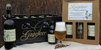 Promotie voor het bier Gageleer. Op een tafel staat een uitgeschonken glas bier met schuimkraag, ernaast een kartonnen geschenkverpakking  met twee flesjes en een glas. Links een bierbak en een grote bruine fles Gageleer. Op de achtergrond kleurt een graanveld oranjebruin.