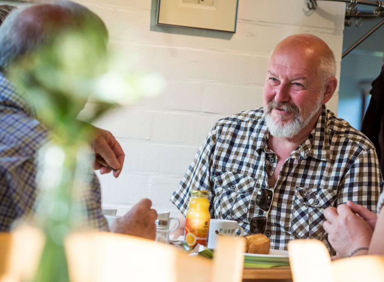 Twee mannen en een vrouw zitten aan een tafel in de cafetaria van Arboretum Kalmthout en genieten van een hapje en een drankje.