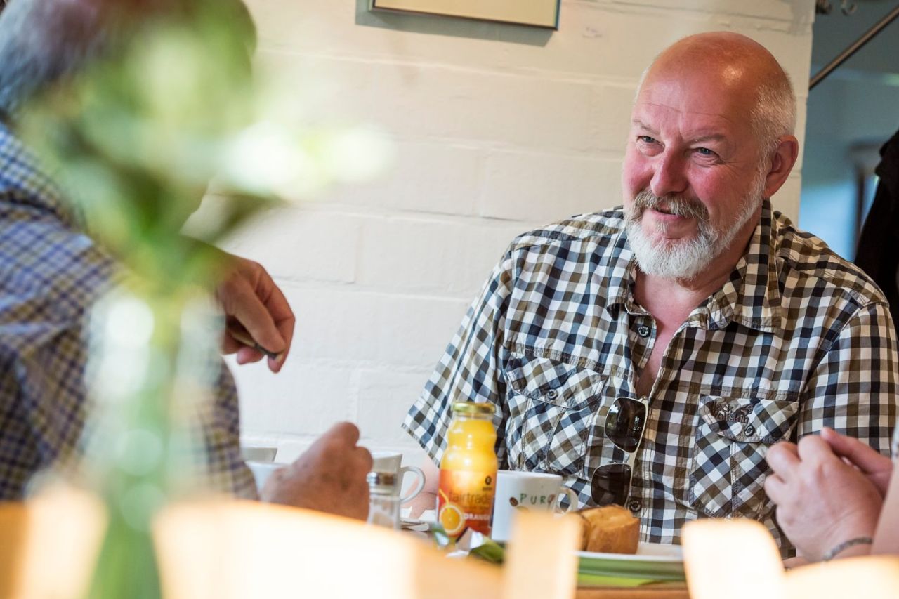 Twee mannen en een vrouw zitten aan een tafel in de cafetaria van Arboretum Kalmthout en genieten van een hapje en een drankje.