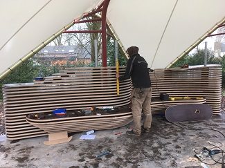 realisatie van een houten wandbank in het paviljoen in de Vlindertuin van Arboretum Kalmthout, organisch gevormde bank bestaande uit verschillende lagen houten platen, met doorkijkeffect.