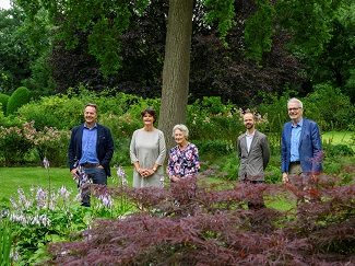 Familie Hubens-Van Laethem poseert samen met de directeur van Arboretum Kalmthout en de gedeputeerde van de provincie Antwerpen in hun tuin met rijkelijke borders en oude bomen op de achtergrond, naar aanleiding van de verkoop van hun domein aan Arboretum Kalmthout en Provincie Antwerpen.