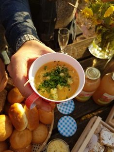 Bovenaanzicht van een herfstige picknicktafel, close-up van een hand die een kop warme soep vasthoudt, broodjes, gebak, fruitsap en bloemen in een vaas staan op de picknicktafel.